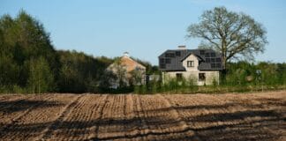 Dom energooszczędny z panelami słonecznymi przy zaoranym polu wiosną